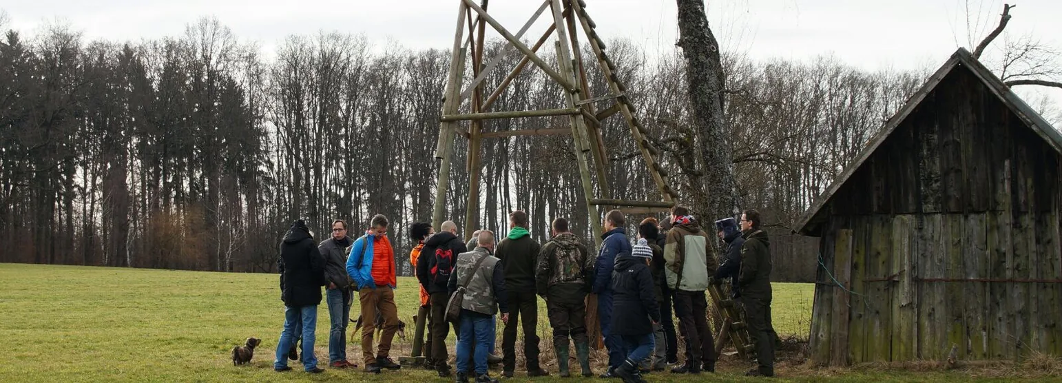 Kursgruppe steht am Waldrand vor einer hölzernen Hochsitzkanzel, rechts daneben eine alte Feldscheune