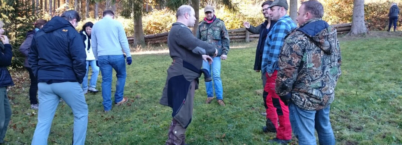 Kursgruppe auf einer Wiese am Waldrand, in der Mitte erklärt ein Ausbilder etwas