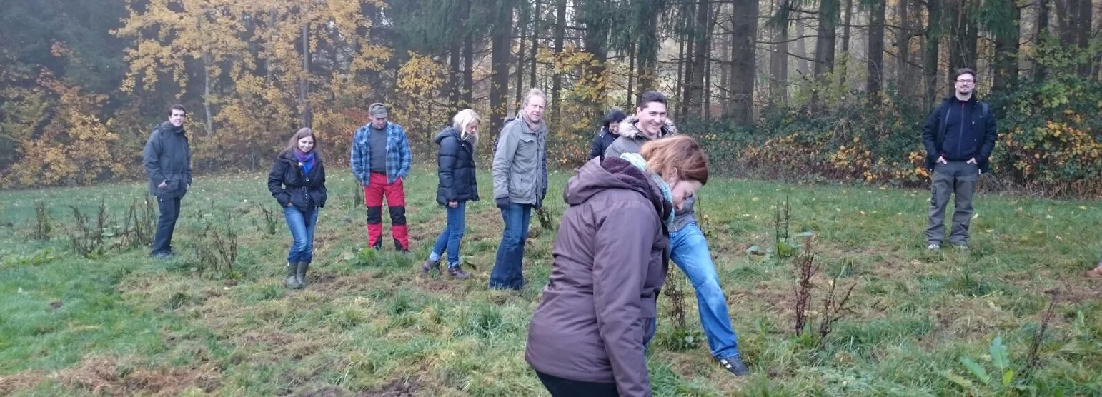 Kursgruppe steht bei Nebel auf einer Wiese vor dem herbstlichen Waldrand