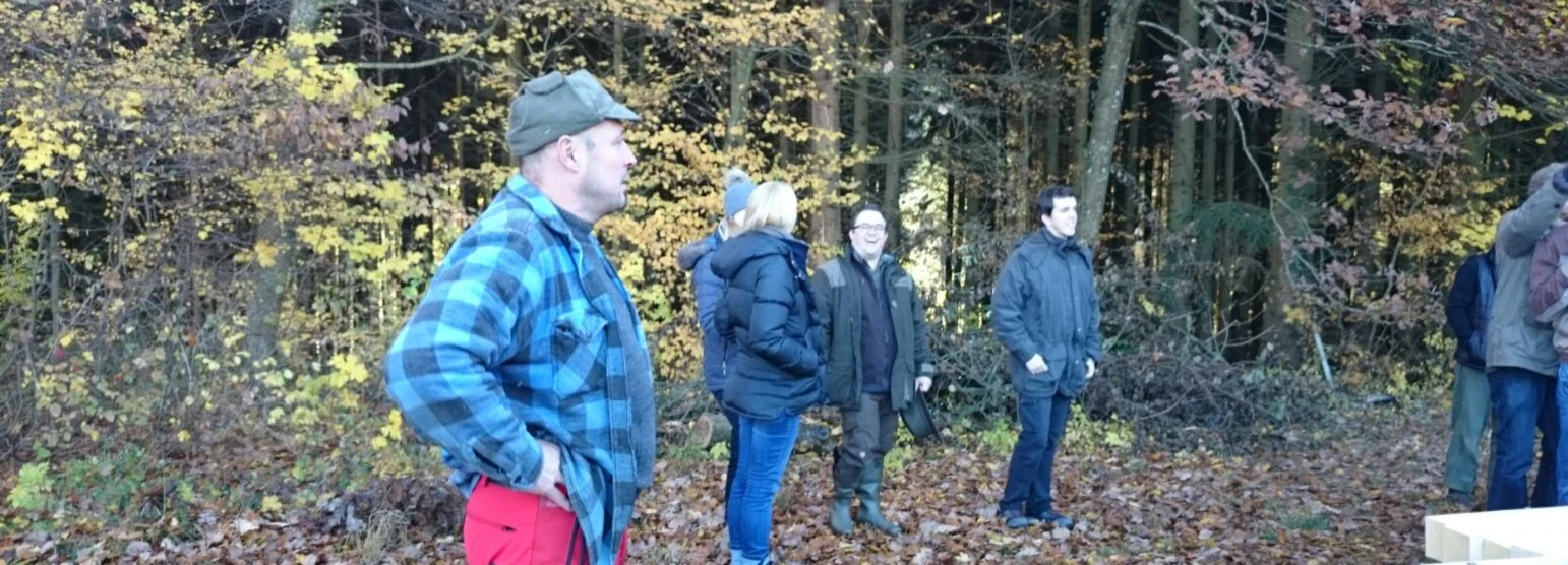 Kursgruppe steht im herbstlichen Laubwald beieinander