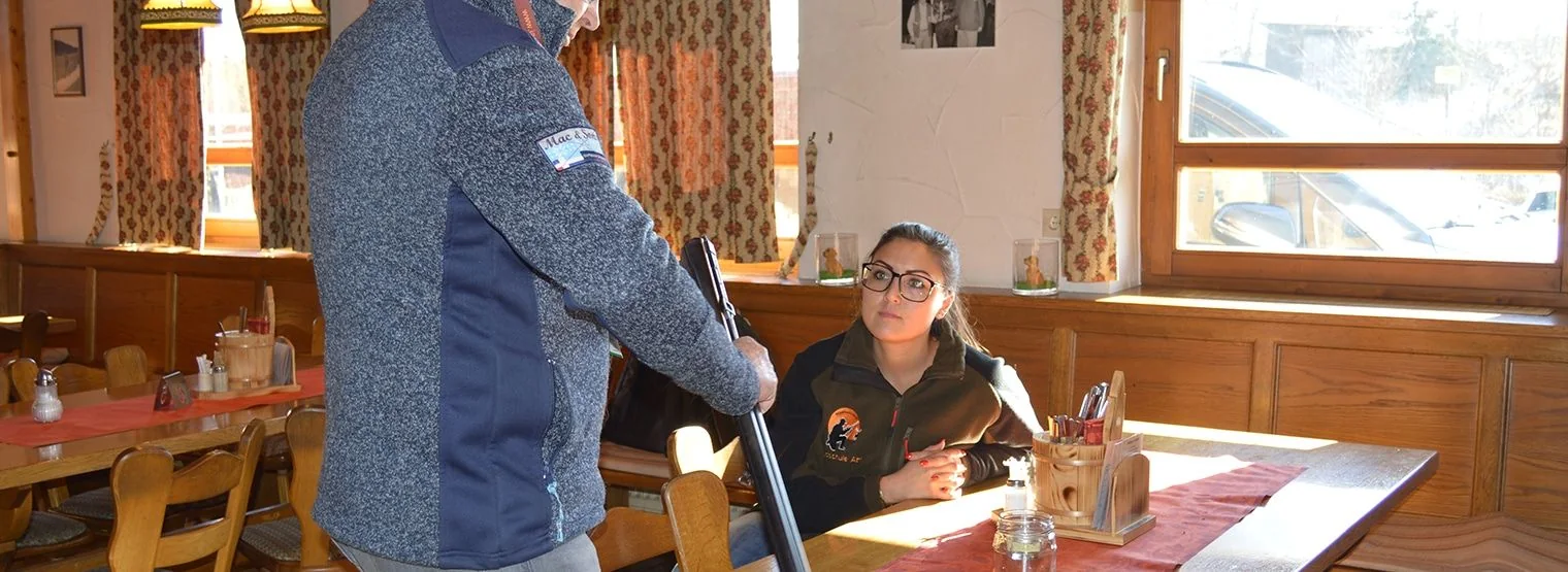 Eine Langwaffe wird über einem Tisch im Schulungsraum gezeigt, eine Teilnehmerin schaut zu