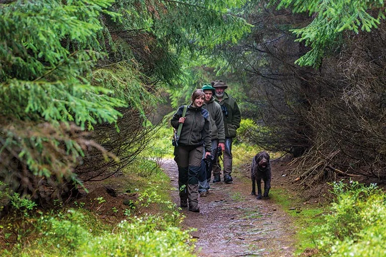 Gruppe in Jagdkleidung geht mit einem Hund über einen Waldweg