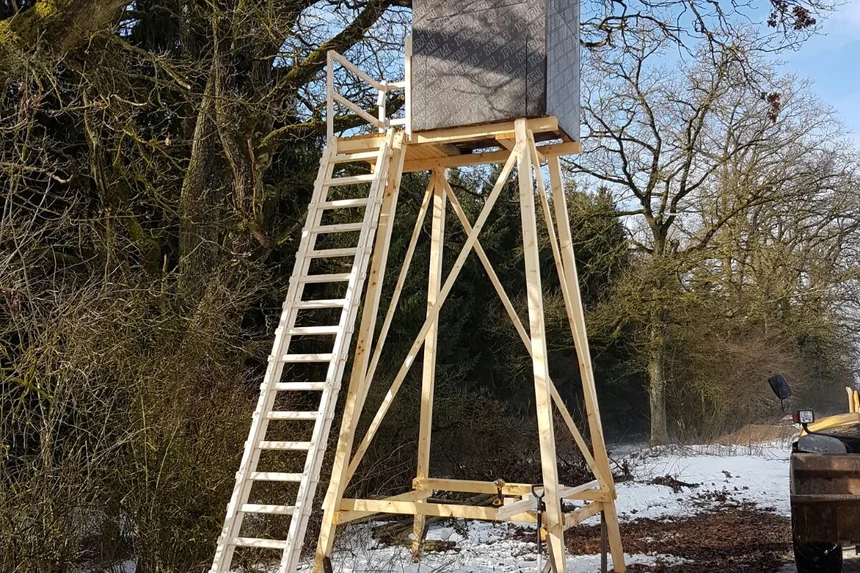 Hölzerner Hochsitz mit Leiter in einem kahlen Wald, Schnee auf dem Boden