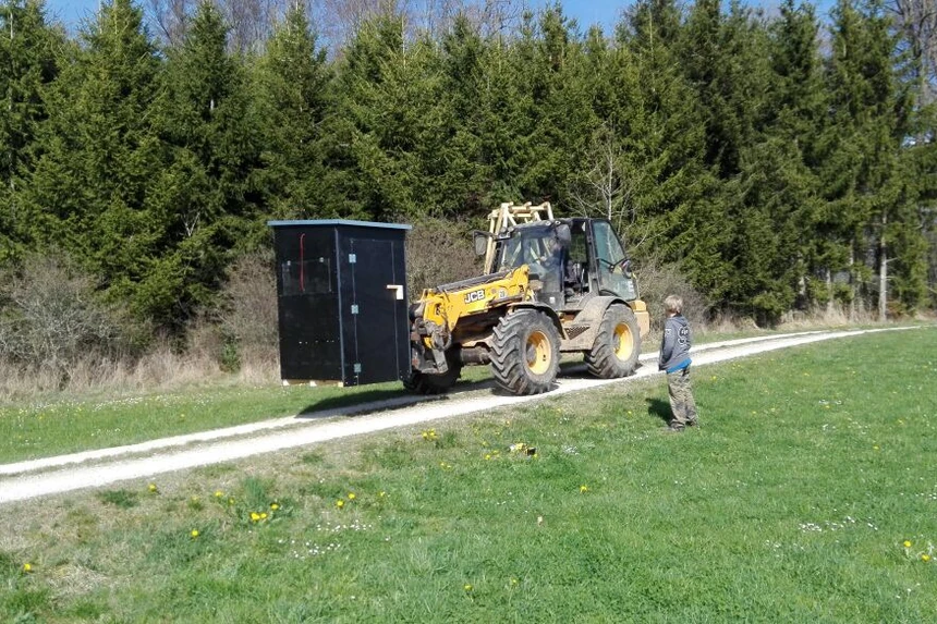 Teleskoplader trägt eine fertige Kanzel über einen Feldweg, daneben geht ein Teilnehmer