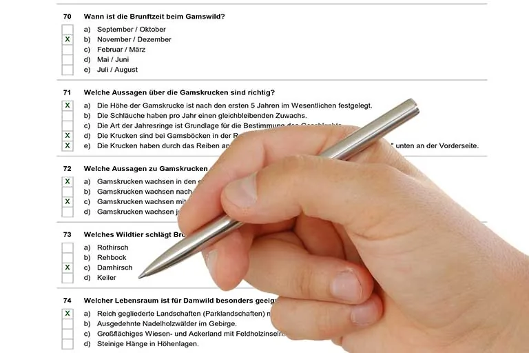 Ausgefüllter Prüfungsbogen mit Multiple-Choice-Fragen zu Gams- und Damwild, daneben eine Hand mit Stift