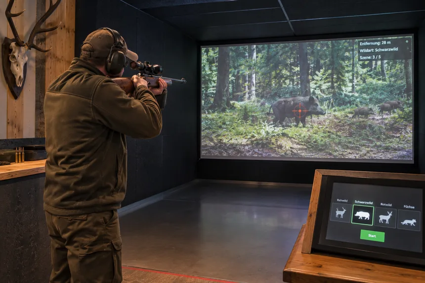 Schütze legt im Schießkino auf eine projizierte Wildschweinszene an, davor ein Bedienpult