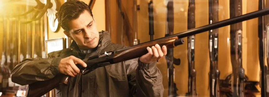 Mann prüft eine gebrochene Bockflinte vor einer Reihe von Langwaffen im Ständer