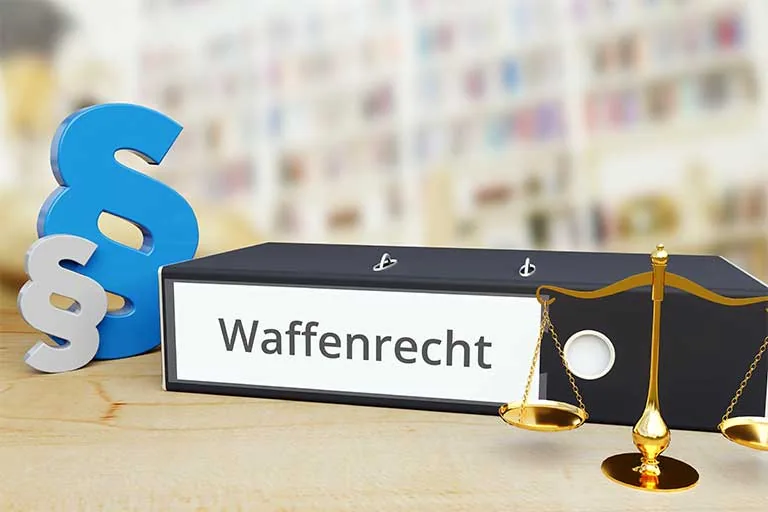 Aktenordner mit der Aufschrift „Waffenrecht“, daneben Paragrafenzeichen und eine Waage