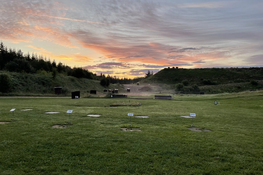 Leerer Wurfscheibenstand im Abendlicht, im Gras die Platten der Schützenstände mit ihren Schildern