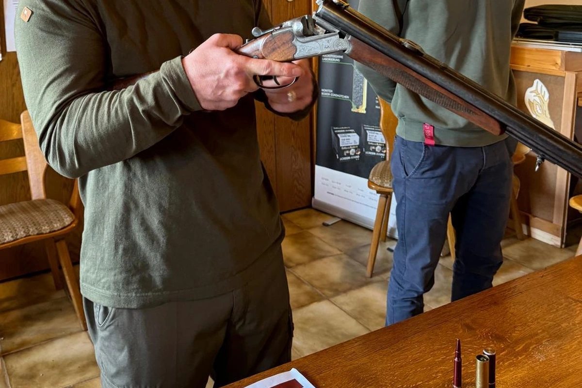 Hände an einer geöffneten Bockflinte im Unterrichtsraum, auf dem Tisch stehen Patronen